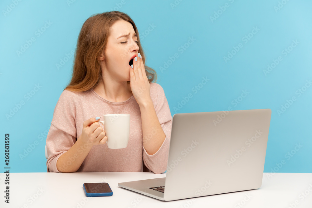 Exhausted drowsy woman sitting at workplace with laptop and yawning feeling sleepy, holding cup coffee to wake up, lazy inefficient employee at work. indoor studio shot isolated on blue background Exhausted drowsy woman sitting at workplace with laptop and yawning feeling sleepy, holding cup coffee to wake up, lazy inefficient employee at work. indoor studio shot isolated on blue background