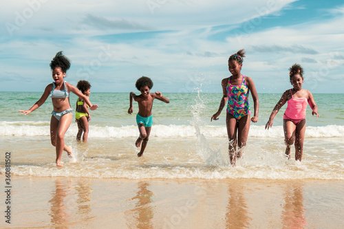 African American children smiley fun run at beach on summer holiday. 