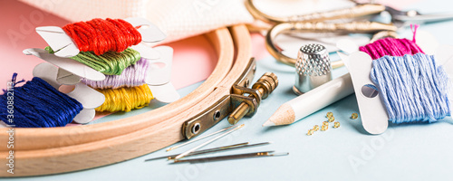 Embroidery set fot cross stitching. White fabric, embroidery hoop, colorful threads, scissors and needls. On blue background. Hobbies concept. Banner