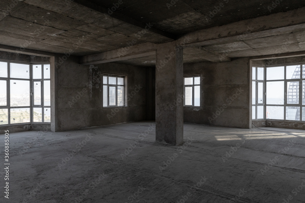 Large spacious room, illuminated by natural light from windows. Unfinished building interior. Repairs in the apartment. Empty dark abstract concrete interior.