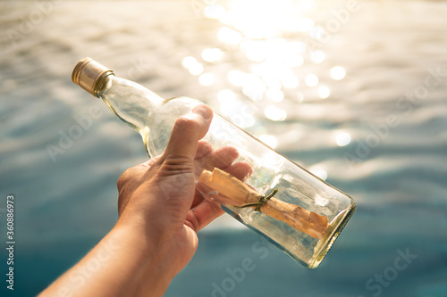 Man holds in his hand a bottle with a message on the background of the sea photo