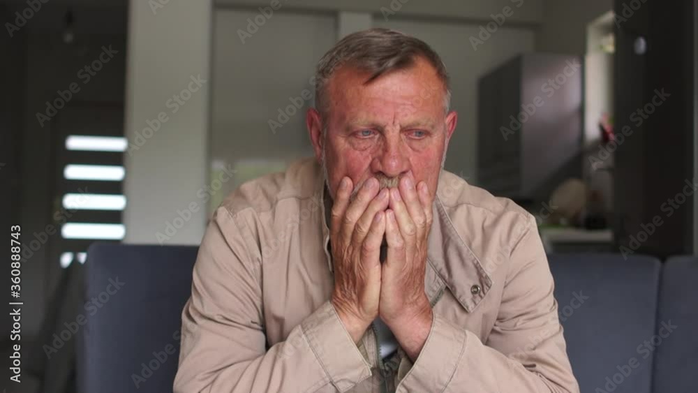 The man is saddened by the dismissal from work. Sad gray-haired worker sitting at home on the couch. The economic crisis and unemployment. Revenue decline The man is saddened by the dismissal from work. Sad gray-haired worker sitting at home on the couch. The economic crisis and unemployment. Revenue decline