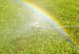 Lawn water sprinkler spraying water over lawn green fresh grass.