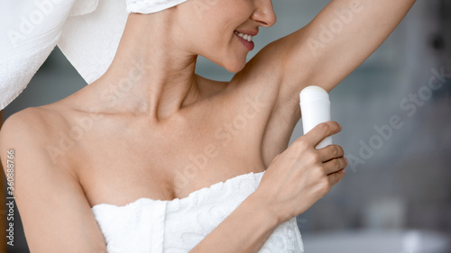 Close up of smiling young woman use deodorant for armpit after shower or bathroom  happy millennial female wrapped in white towel apply dry antiperspirant  perform daily body treatment at home