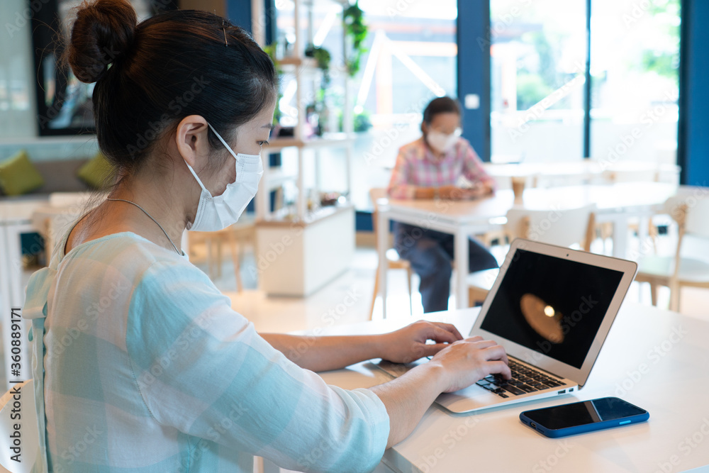 Obraz premium Asian woman wearing face mask and keep social distanicng by sitting on each table in the restaurant during covid-19 or coronavirus outbreak. new normal lifestyle concept
