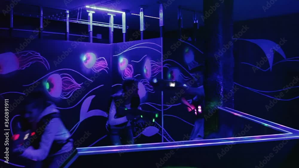 Ordinary Laser tag players young mens and womens playing in teams in dark laser tag station