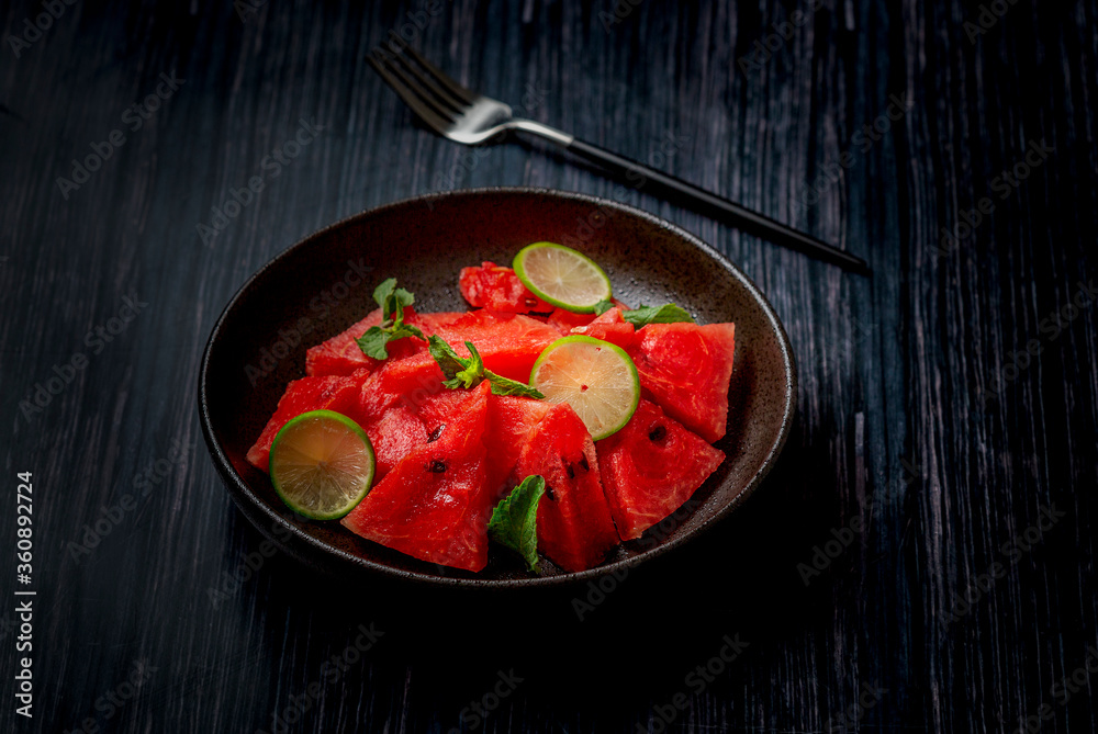 watermelon slices mixed with mint leaves and lemon slices in a black ceramic plate