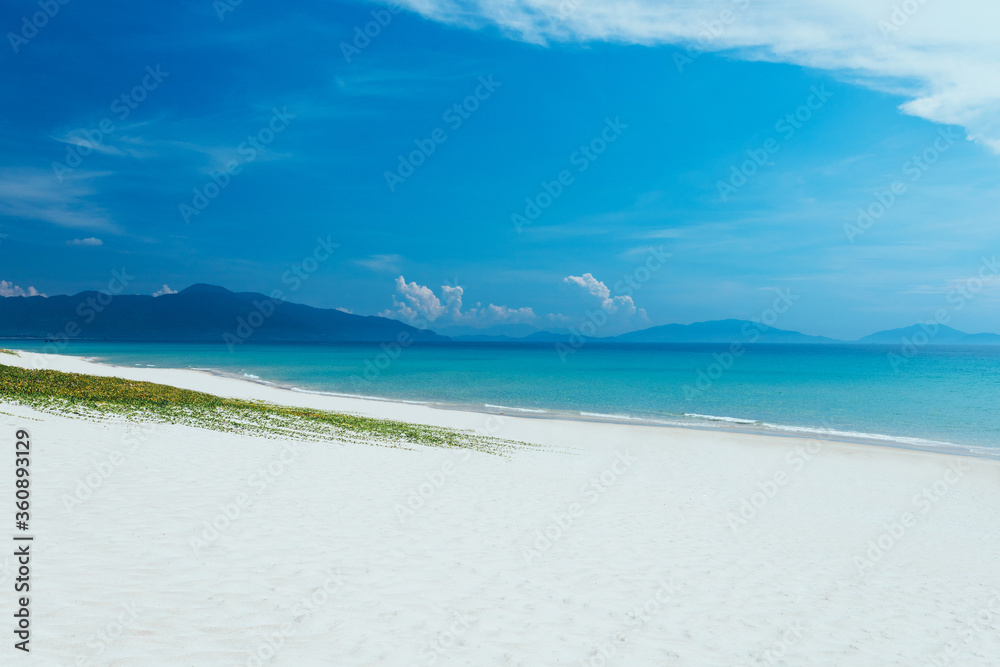 view of sandy sea beach. Calm waves, foam. Blue sky with white clouds. An empty long beach, ocean and mountain background