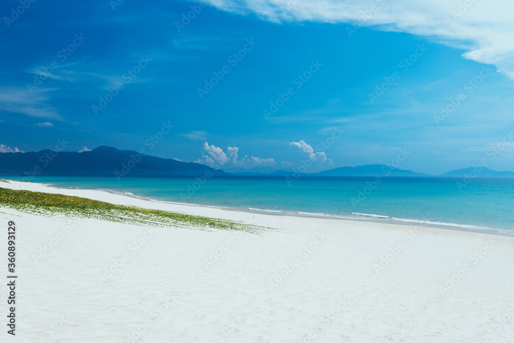view of sandy sea beach. Calm waves, foam. Blue sky with white clouds. An empty long beach, ocean and mountain background view of sandy sea beach. Calm waves, foam. Blue sky with white clouds. An empty long beach, ocean and mountain background
