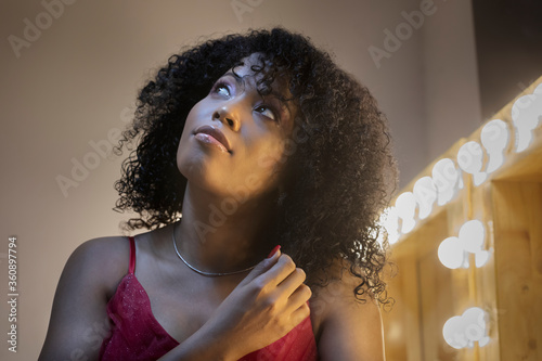 beautiful african american and afro cuban singer sitting looking up in her dressing room before a performance. She has afro hair and a red dress photo