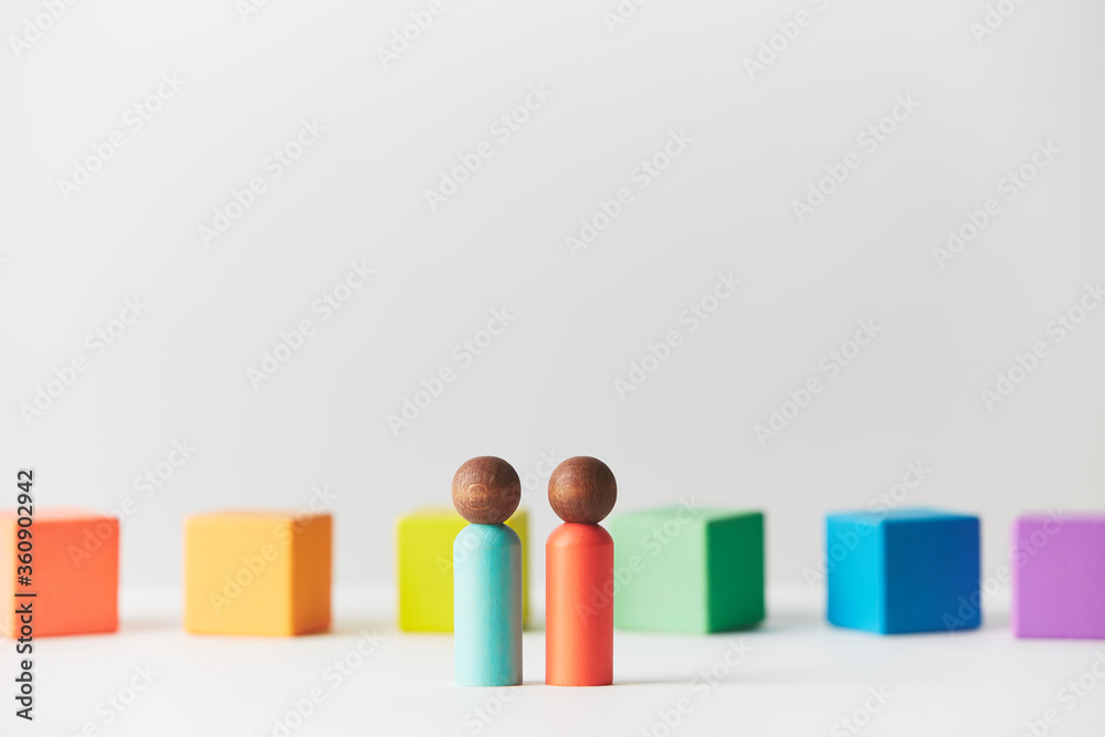 Wooden figures concept. Couple standing in front of wooden blocks in colours of the gay pride rainbow flag. Couple of dark skin colour. Wooden figures concept. Couple standing in front of wooden blocks in colours of the gay pride rainbow flag. Couple of dark skin colour.