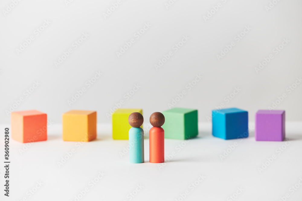 Obraz premium Wooden figures concept. Couple standing in front of wooden blocks in colours of the gay pride rainbow flag. Couple of dark skin colour. 