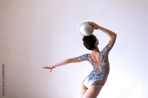 Girl gymnast doing exercise with silver ball (back view) photo