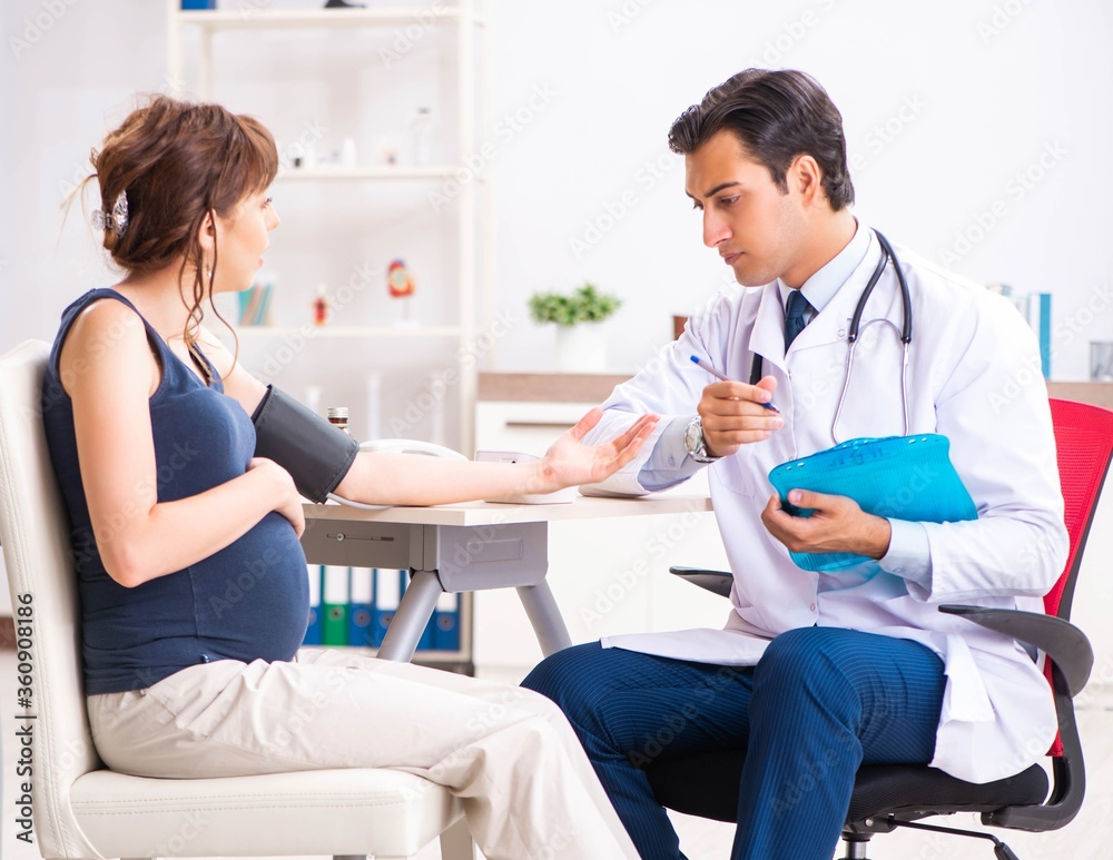 Fototapeta premium Young doctor checking pregnant woman's blood pressure