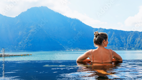 Young woman relax in infinity pool with lake view. Natural hot spring spa under Batur volcano. Travel in Kintamani, Bali. Healthy lifestyle, recreational activity on family summer holiday. © Tropical studio