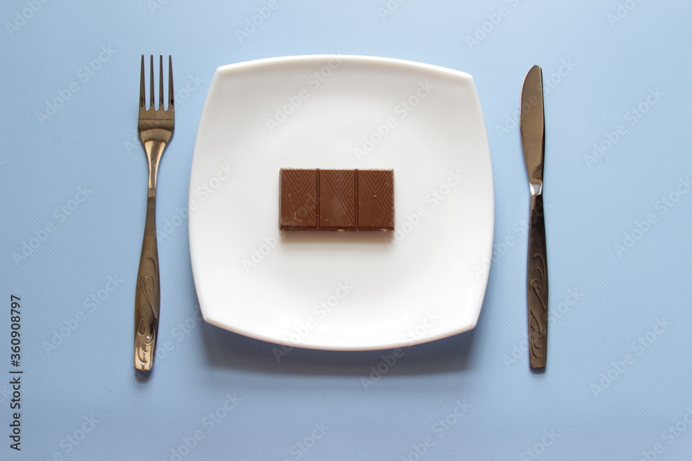 Fork, knife and white plate with chocolate over blue background. Clean plate and cutlery on light background. Top view. Fork, knife and white plate with chocolate over blue background. Clean plate and cutlery on light background. Top view.