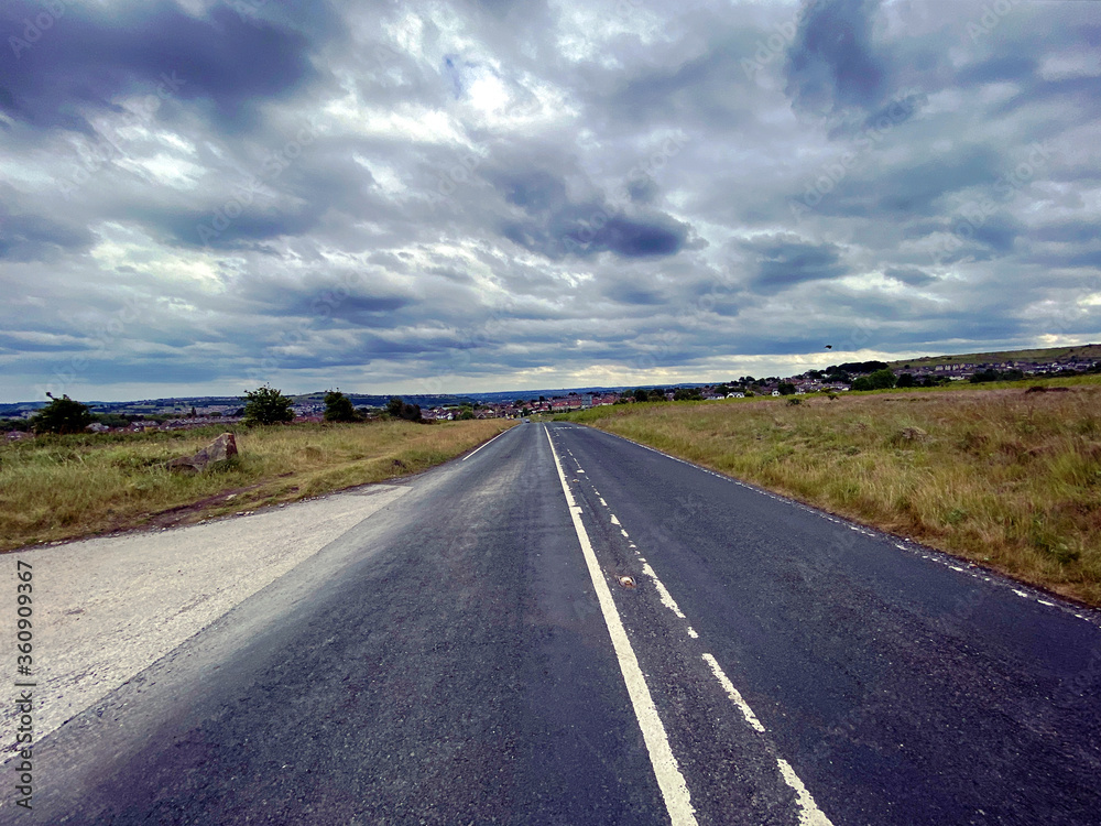 Fototapeta premium Main road, leading across the moor, into Baildon town, with heavy cloud above,