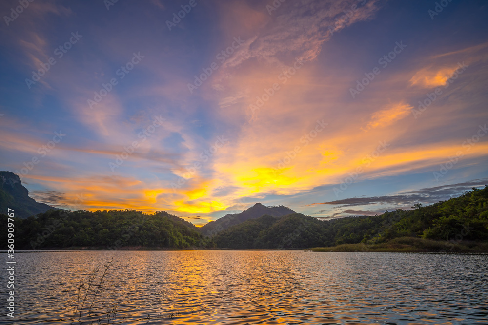 Beautiful sunset on lake with sun setting down behind the mountain and reflected on the water surface..