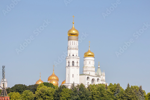 View of Ivan the Great Bell Tower above green trees on a summer morning in Moscow, Russia. It's a church tower inside the Moscow Kremlin complex. Clear blue sky. Theme of travel in Russia.