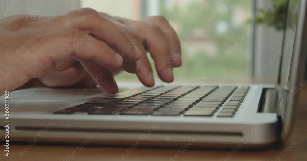 Hands of a man typing text on a beech laptop keyboard. Person sitting at the wooden desk Working He, types, writes emails, Surfs the Internet, Designs Software Hands of a man typing text on a beech laptop keyboard. Person sitting at the wooden desk Working He, types, writes emails, Surfs the Internet, Designs Software