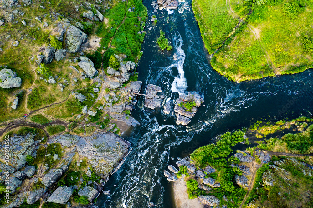 swirling streams of mountain river with a rocky shore in a beautiful valley in forest, top view.
