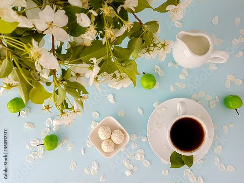 A cup of coffee with sweets on the background of flowering branches of apple trees.