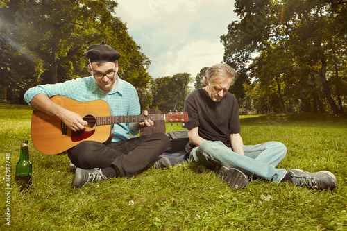 Two men on city park summer meadow enjoying day with guitar