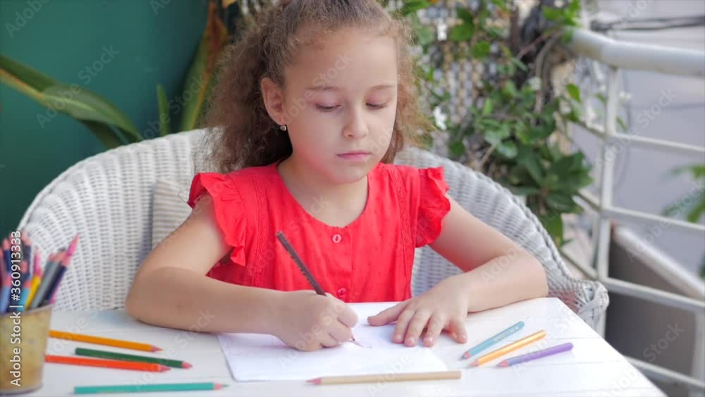 Happy Little Girl or Cute primary child school child of 7-8 years old at home relaxing sits in house and paints on paper use colour pencils. Child draws,focused children elementary education concept. Happy Little Girl or Cute primary child school child of 7-8 years old at home relaxing sits in house and paints on paper use colour pencils. Child draws,focused children elementary education concept.