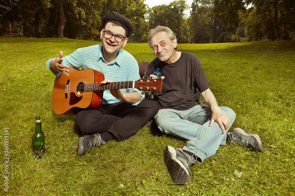 Two men on city park summer meadow enjoying day with guitar Two men on city park summer meadow enjoying day with guitar
