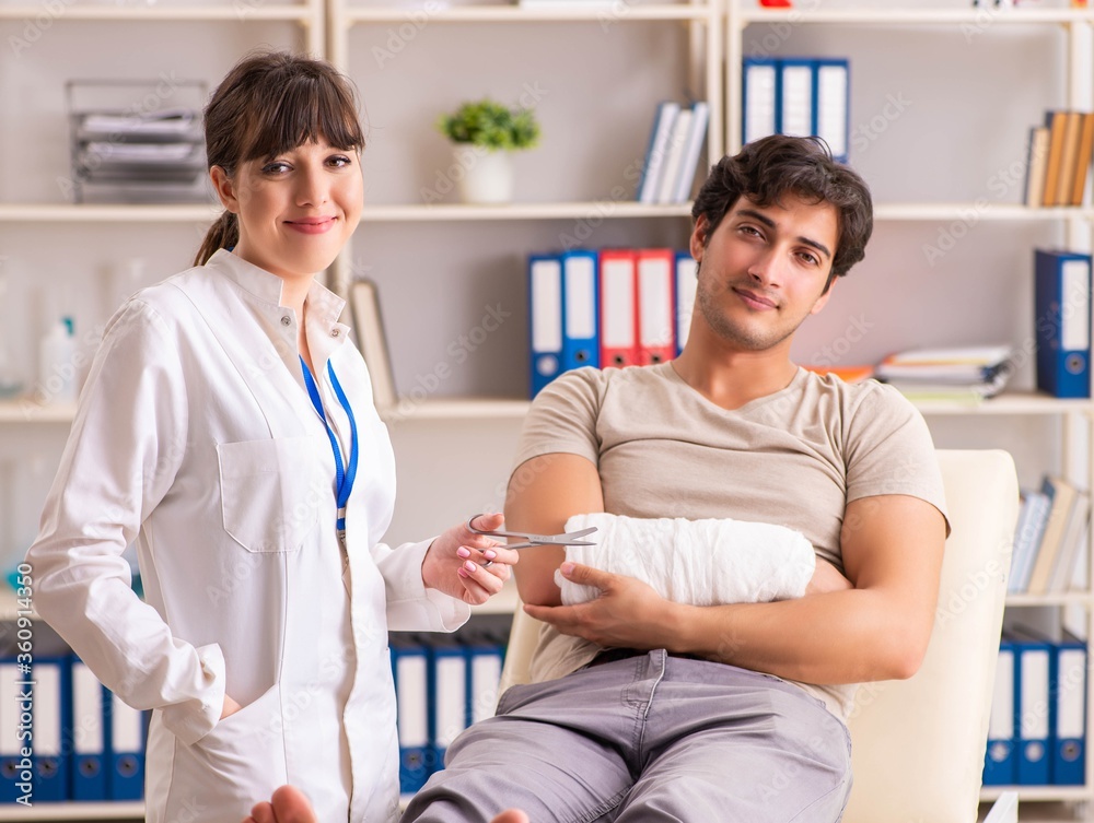 Fototapeta premium Young man with bandaged arm visiting female doctor traumatologis