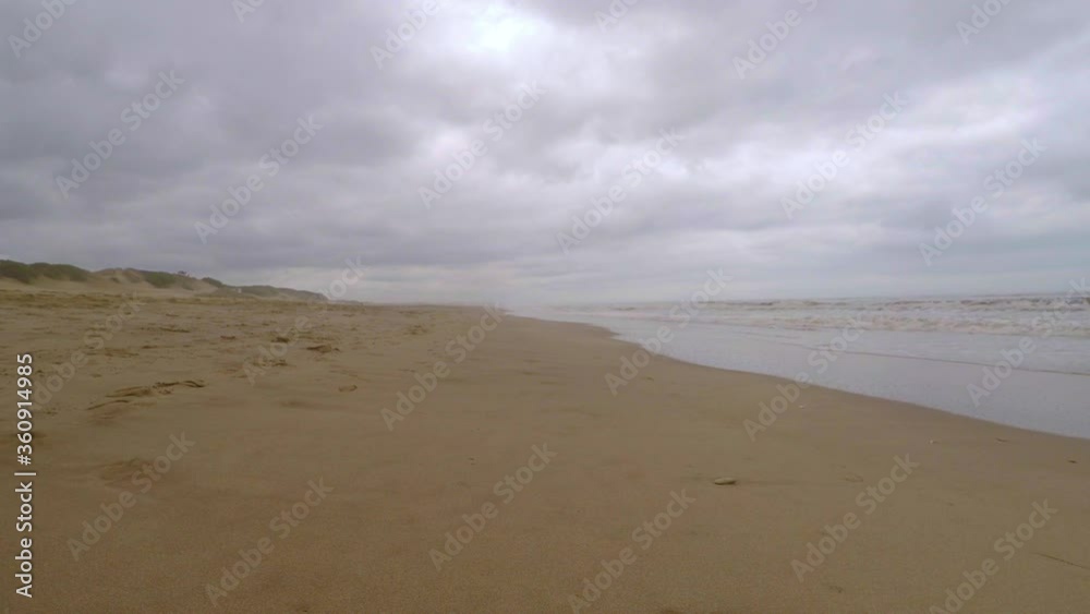 Walking in the sand of an empty lonely beach during a cloudy day, aside the sea waves Walking in the sand of an empty lonely beach during a cloudy day, aside the sea waves