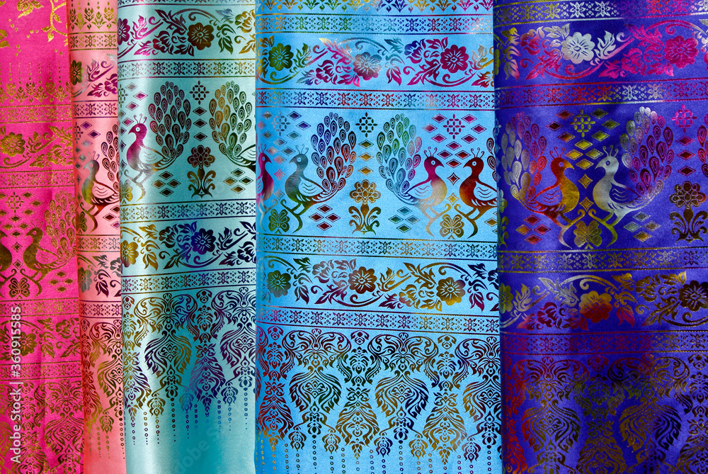 Lengths of colorful silk fabric with a peacock and floral motif for sale at an open-air market in Xishuangbanna, Yunnan Province, China Lengths of colorful silk fabric with a peacock and floral motif for sale at an open-air market in Xishuangbanna, Yunnan Province, China