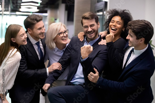 Excited business man with happy coworkers congratulating with success. Cheerful team around joyful boss. Mix race workers supporting leader with great news celebrating achievement or promotion
