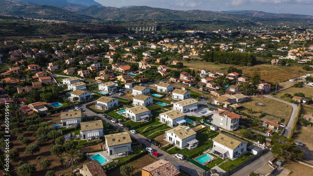 Aerial view of the Villa in Campofelice di Roccella in Sicily, under a beautiful sunny sky, with swimming pools and trees.