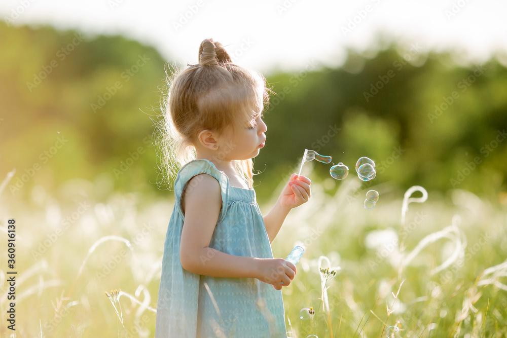 Little girl inflates soap bubbles in summer on a walk