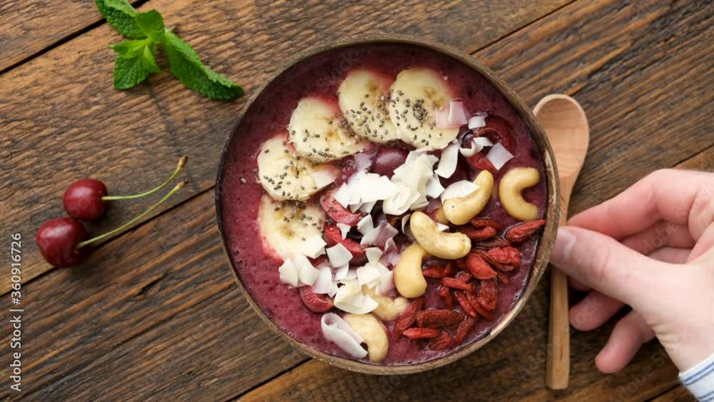 Male hands serving superfood acai smoothie bowl with toppings in coconut bowl. Top view. Vegan paleo diet concept