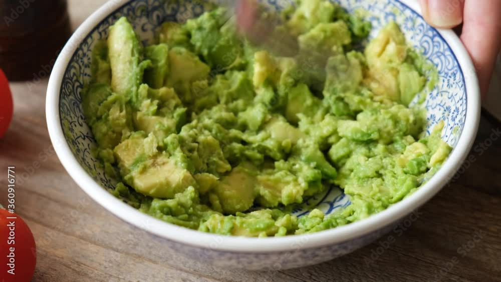 Mashing ripe avocado with fork in a bowl. Closeup view of preparing avocado mash sauce guacamole Mashing ripe avocado with fork in a bowl. Closeup view of preparing avocado mash sauce guacamole