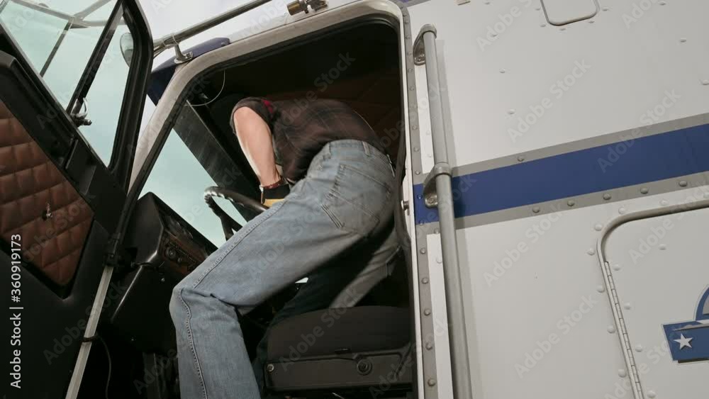 Male Semi Truck Driver Climbing To Vehicle Cabin Holding On To Railing And Inserting Key In Ignition Switch. 