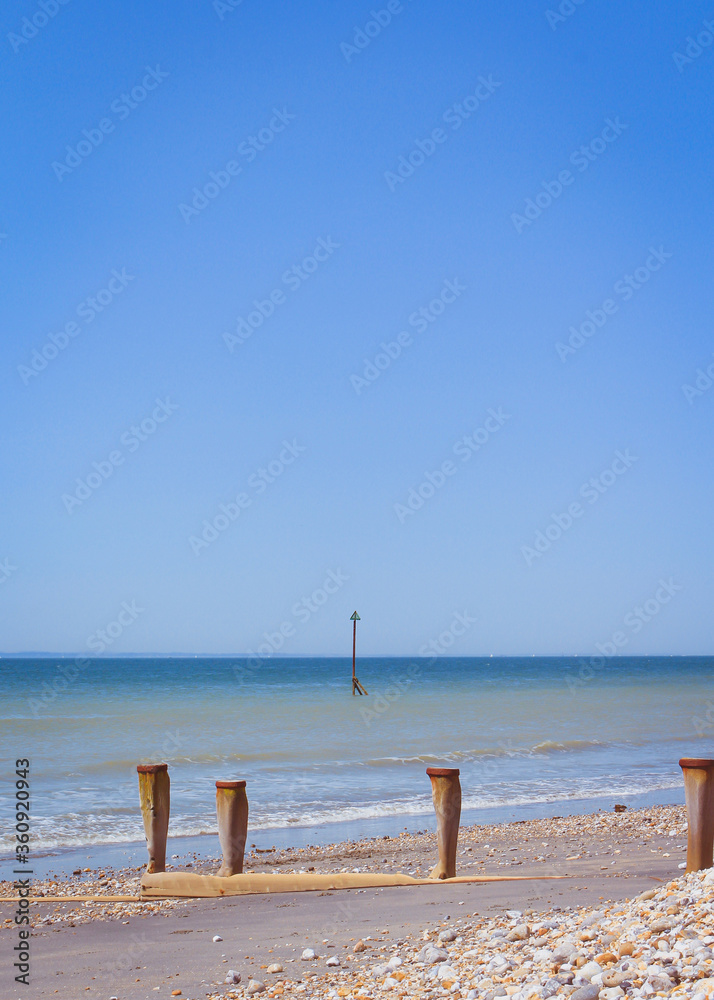 Morning summer beach with blue water and clear blue sky, coloured pebbles on the beach sand, waves in the ocean.
