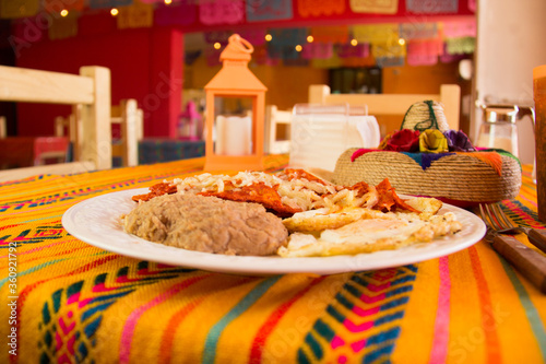 Huevos estrellados con chilaquiles y frijoles refritos puestos en una mesa de una restaurante con un ambiente mexicano