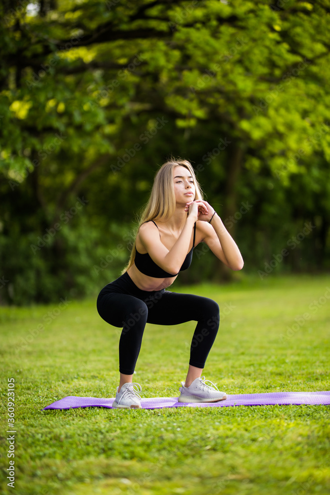 Young woman practicing squats in park. Young woman exercising outdoors on a nice summer day.