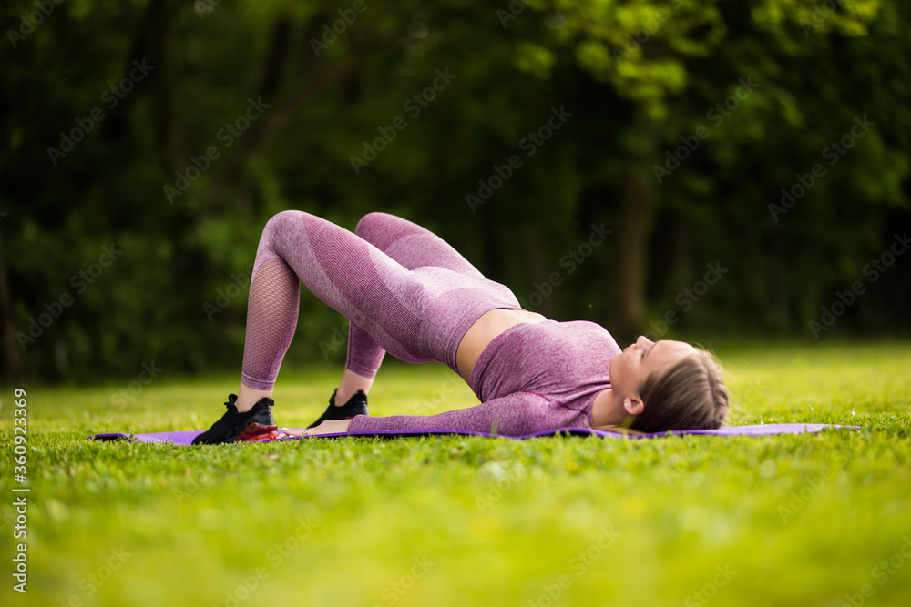 Fototapeta premium Fit woman doing abdominal crunch and training outside on green grass at park. Fitness, sport and healthy lifestyle, abs workout