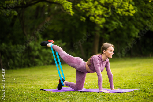 Athletic woman workout with resistance band outdoors. Fitness girl doing exercise for glutes at the park photo