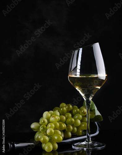 Wine background. White wine in wineglass, grape on old bottle .