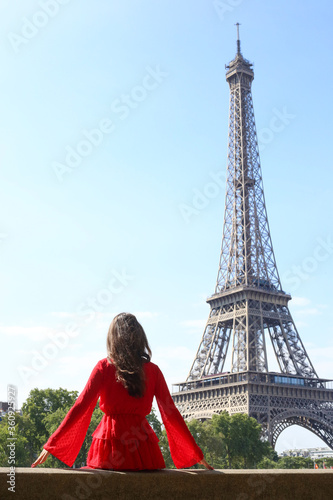 Girl in red dress sitting with her back in front of Eiffel tower in Paris in summer © Oksana