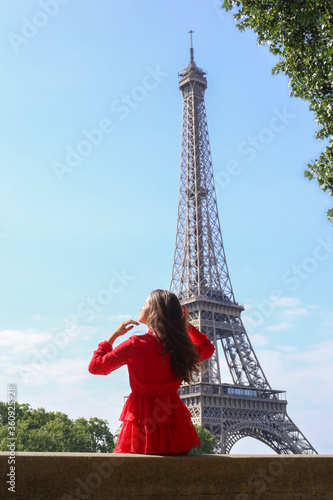 Young girl in red dress sits alone in front of Eiffel Tower in Paris on summer sunny day © Oksana