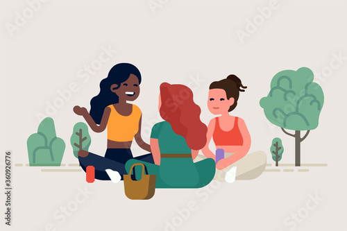 Three girl friends having a picnic in a park sitting around talking to each other