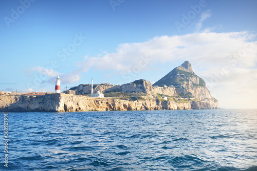Trinity lighthouse at the rocky shore (cliffs) of the Europa Point. British Overseas Territory of Gibraltar, Mediterranean sea.A view from the yacht. National landmark, sightseeing, travel destination