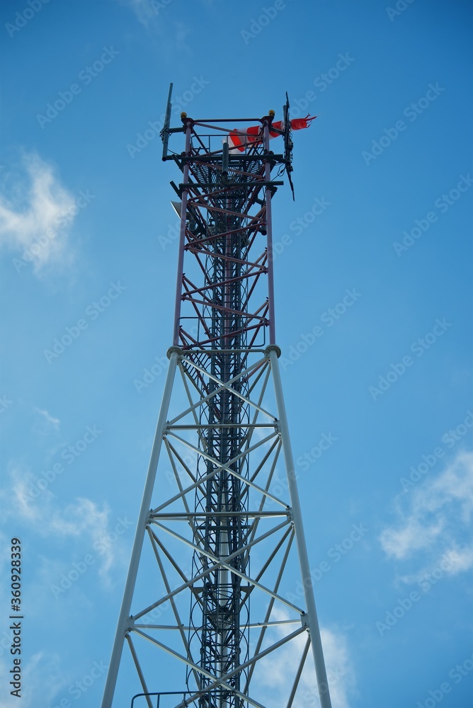Communication tower on a background of blue sky. A weather vane at the very top indicates the direction of the wind. The image of freedom. Communication tower on a background of blue sky. A weather vane at the very top indicates the direction of the wind. The image of freedom.