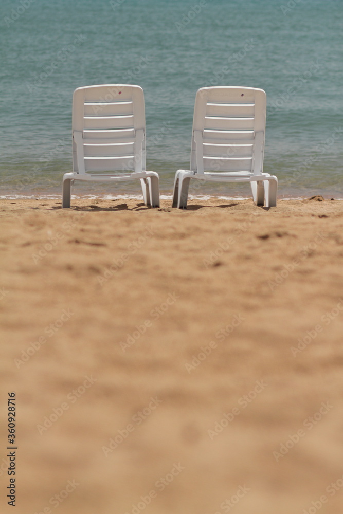 Deck chair in the sand on the shore. Relax, relaxation on the beach. Blue water in the ocean sea. Deck chair in the sand on the shore. Relax, relaxation on the beach. Blue water in the ocean sea.